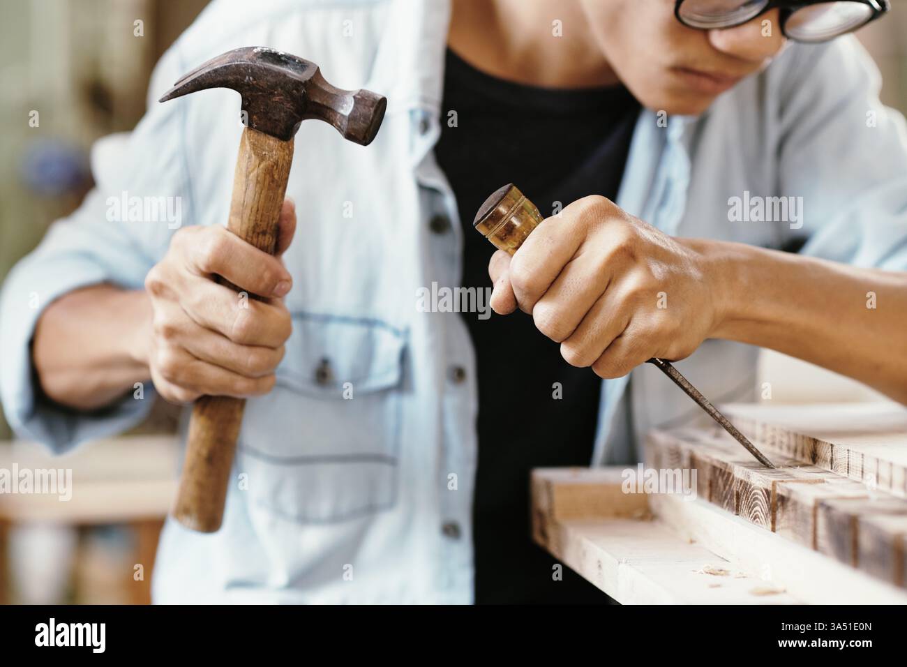 Primo piano di un falegname che intaglia legno di noce con martello e scalpello su un banco da lavoro. Ideale per la lavorazione del legno, l'artigianato e la grafica professionale. Foto Stock