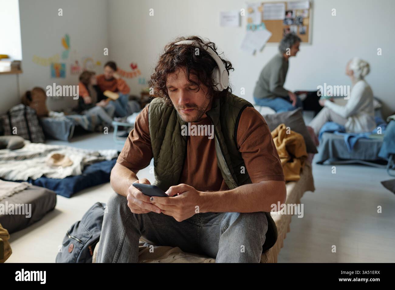 Indossa le cuffie per scorrere le playlist o i video clip online sullo smartphone mentre sei seduto sulla couchette nel campo profughi Foto Stock