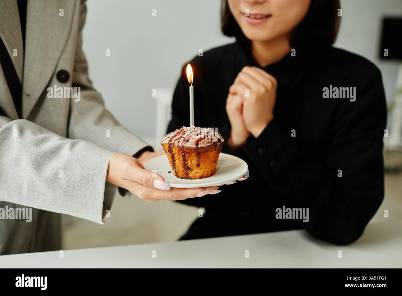 Festeggia le pietre miliari del lavoro di squadra e dell'ufficio con questo primo piano di colleghi che presenta una torta di compleanno a una giovane donna sorridente. Perfetto per comunicazioni aziendali, newsletter interne o campagne di marketing sulla cultura del luogo di lavoro. La torta festiva e la candela offrono un'atmosfera calda e celebrativa in un ambiente interno. Foto Stock