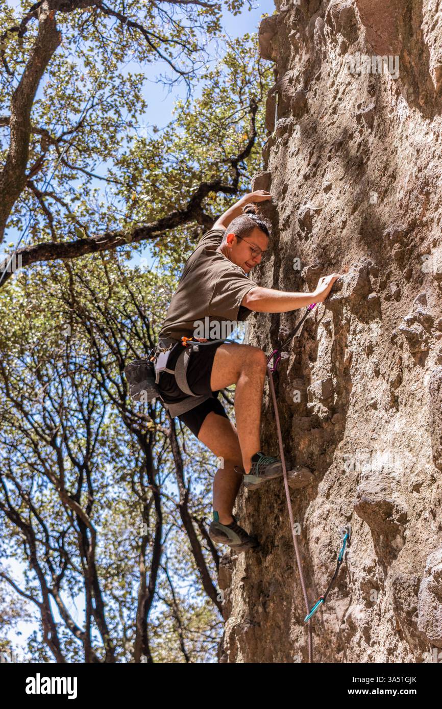 Arrampicatore maschile che sale su una scogliera con attrezzatura in una giornata di sole in un ambiente naturale. Questa dinamica immagine sportiva all'aperto si adatta a temi di avventura, fitness e arrampicata. Foto Stock