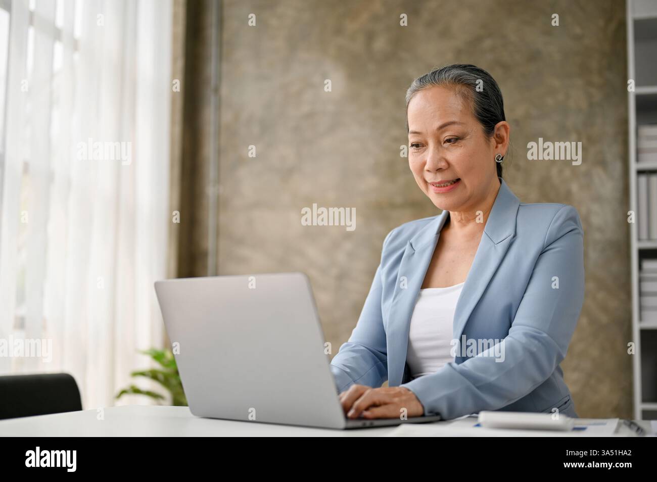 Donna d'affari anziana di successo che utilizza un notebook alla sua scrivania, proiettando attenzione e leadership professionale. L'immagine mette in evidenza l'esperienza, il lavoro aziendale e l'imprenditorialità femminile nelle fasi successive della carriera. Adatto per aziende, dirigenti e donne in argomenti di leadership. Foto Stock