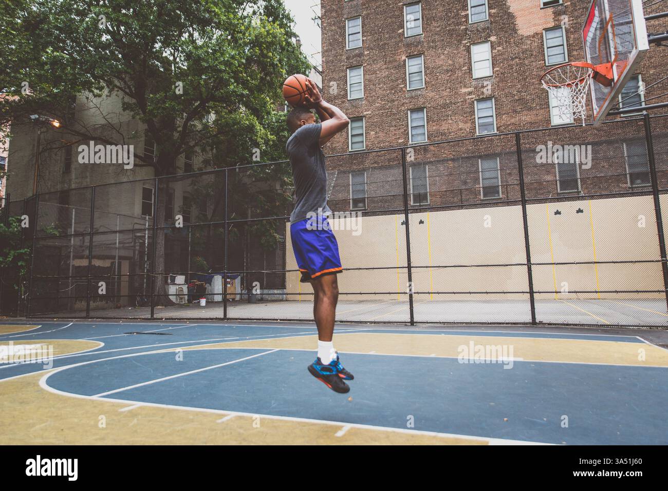 Il giovane giocatore afroamericano si allena su un campo urbano di New York City. Questa immagine sportiva dinamica cattura la messa a fuoco, il ritmo di allenamento e l'energia del basket da strada. Foto Stock