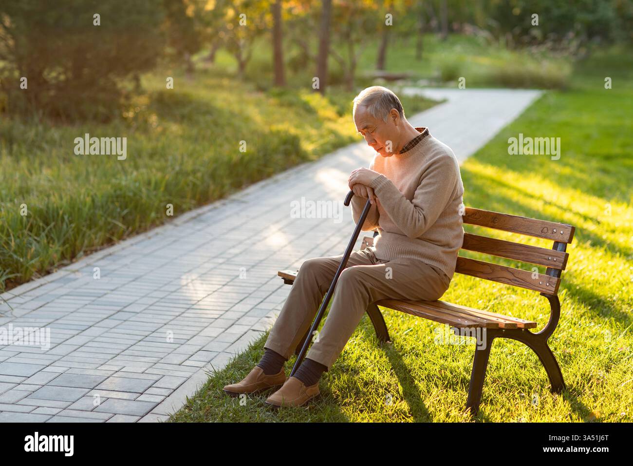 Uomo cinese anziano con un'espressione triste siede su una panchina del parco alla luce del giorno. L'ambiente esterno e i delicati toni autunnali trasmettono solitudine e riflessione. Utile per argomenti su invecchiamento, benessere e vita urbana a Pechino. Foto Stock