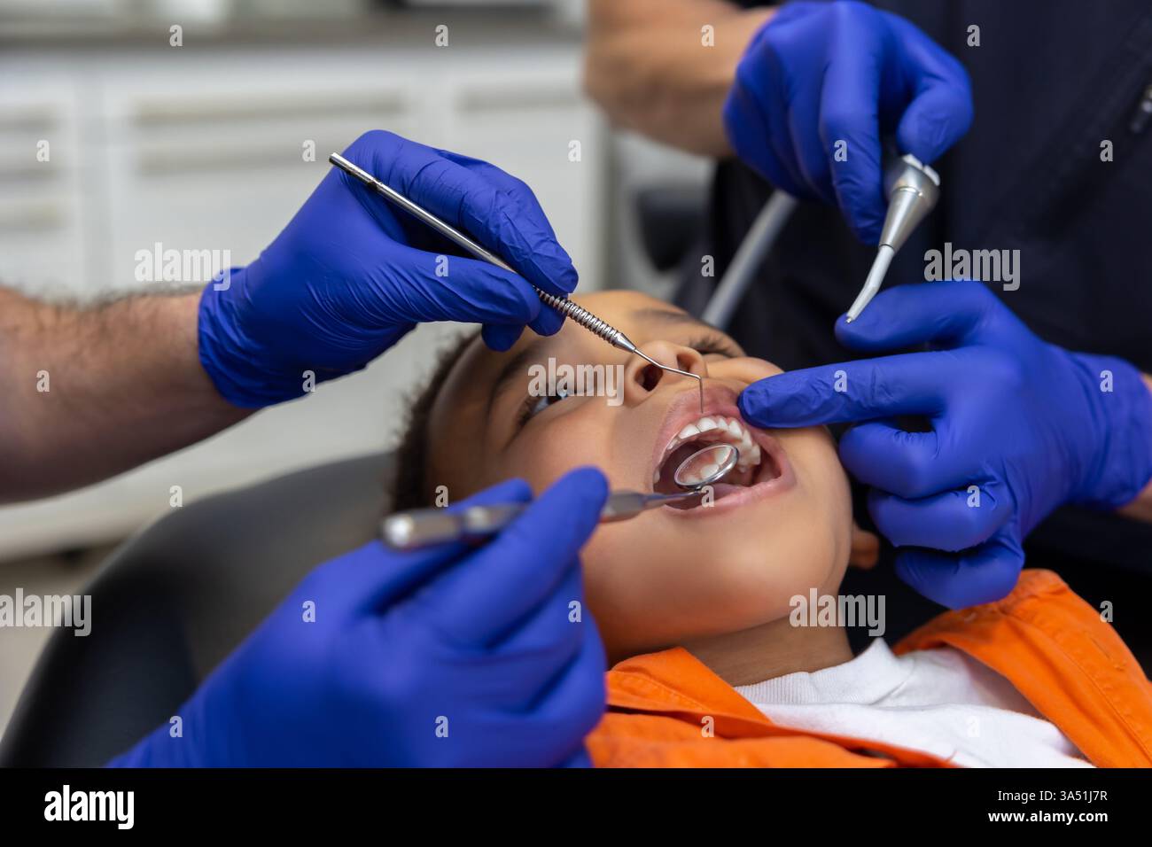 Primo piano di dentisti al lavoro che curano un bambino in una clinica odontoiatrica. L'immagine evidenzia l'odontoiatria pediatrica e l'attenta cura del paziente. Uso per l'assistenza sanitaria, cliniche odontoiatriche e argomenti dentali familiari. Foto Stock