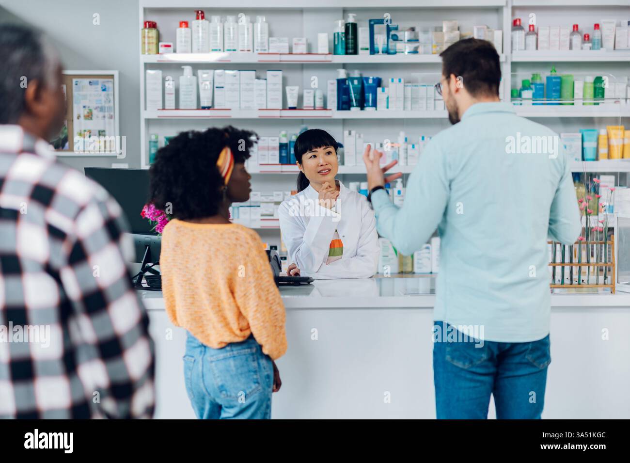 Farmacista giapponese che assiste un cliente con farmaci da prescrizione in una farmacia occupata. Gli scaffali dei prodotti sanitari creano un ambiente farmaceutico autentico. Foto Stock