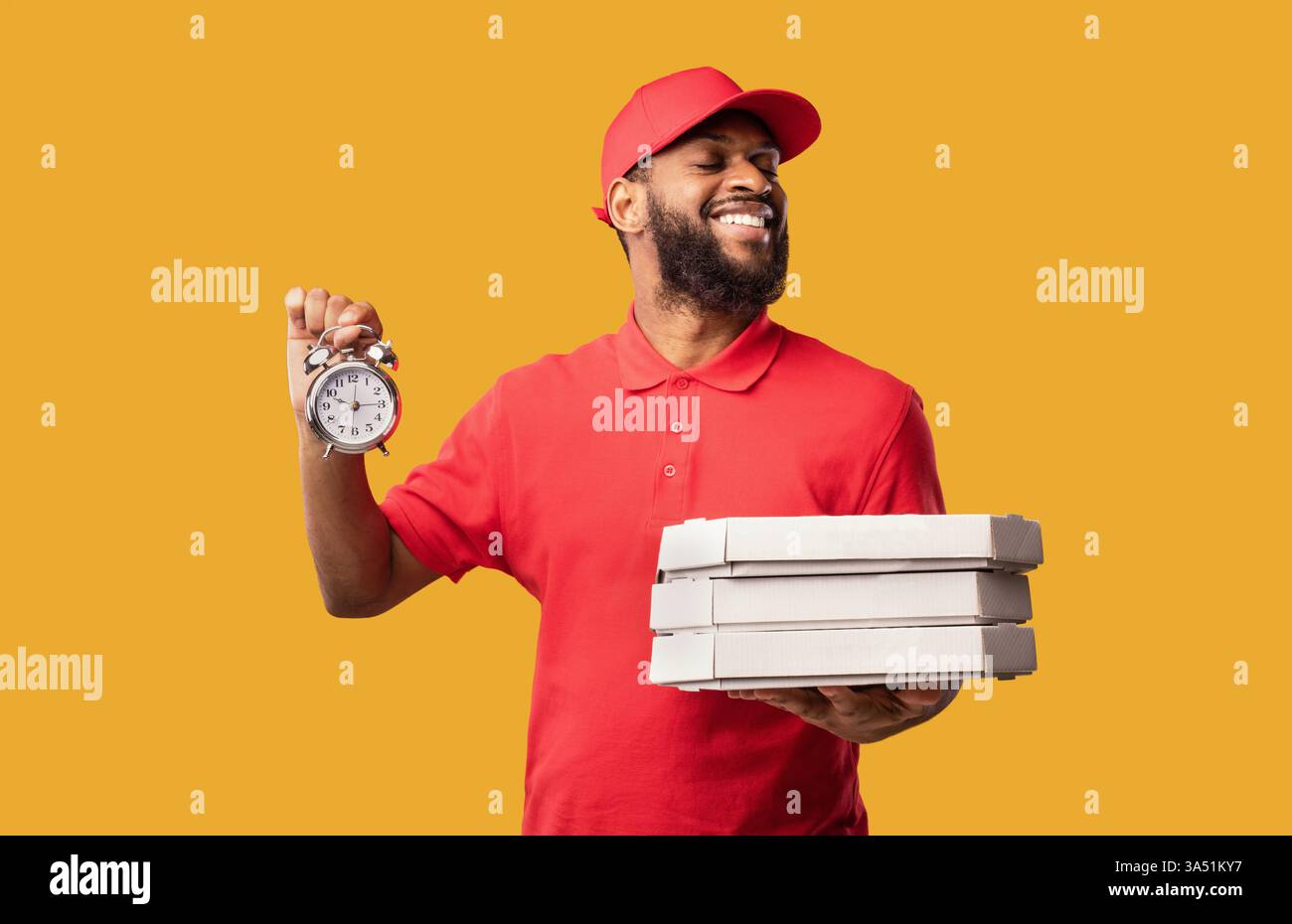 Corriere nero in uniforme professionale con cassette per pizza e orologio su sfondo giallo brillante. Ideale per consegne rapide, servizi di ristorazione e pubblicità tramite corriere. Foto Stock