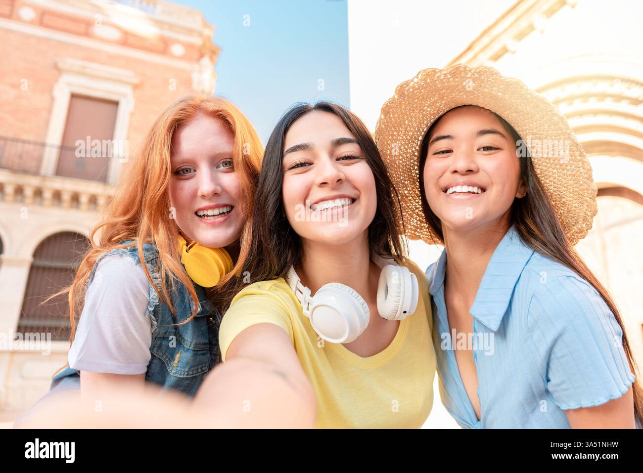 Felice gruppo multirazziale di giovani fidanzate in abiti eleganti scatta un selfie contro gli edifici urbani di Valencia, guardando la fotocamera. Questa allegra immagine di viaggio e amicizia è ideale per la vita in città, lo stile di vita e le campagne sui social media. Foto Stock