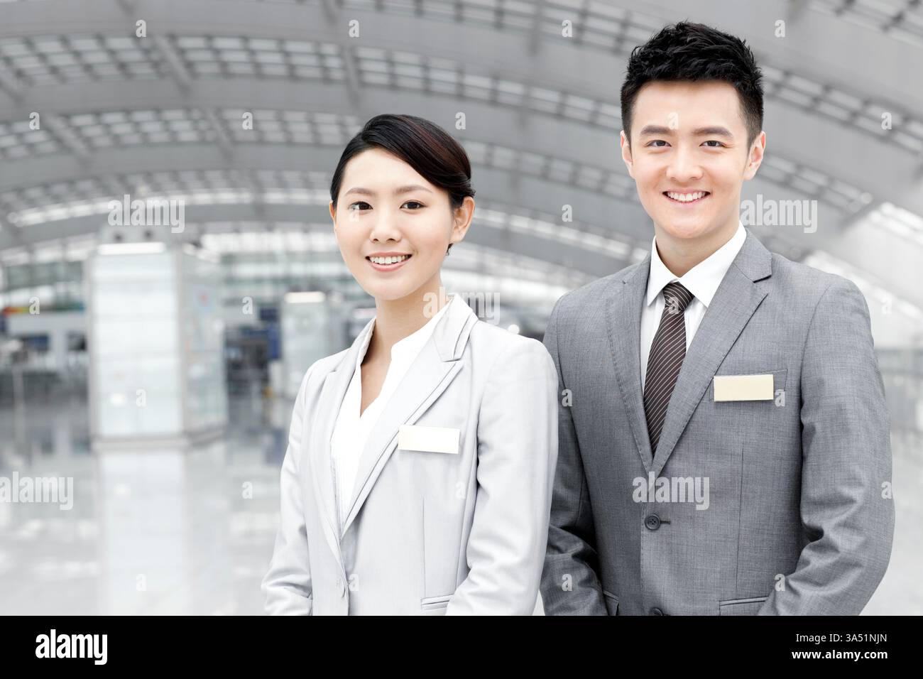 Il personale cinese maschile e femminile dell'aeroporto si trova nella hall dell'aeroporto, pronto ad assistere i viaggiatori. Ideale per gli argomenti relativi al servizio clienti, al lavoro di squadra e all'ospitalità nei centri di viaggio. Una chiara rappresentazione delle operazioni aeroportuali in un ambiente cittadino affollato. Foto Stock