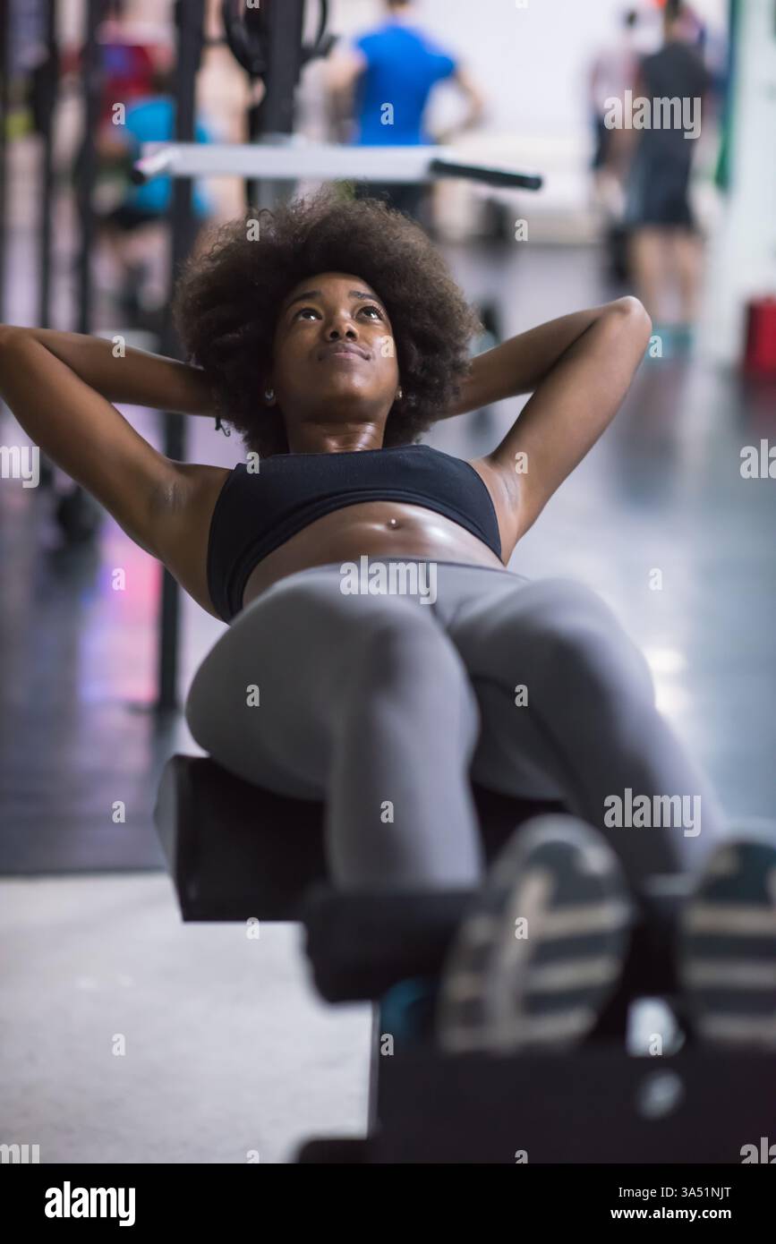 Giovane donna afroamericana che si esibisce sit-up in uno studio di palestra. Mostra allenamento fitness, esercizi principali e uno stile di vita sano per campagne sportive e di benessere. Foto Stock