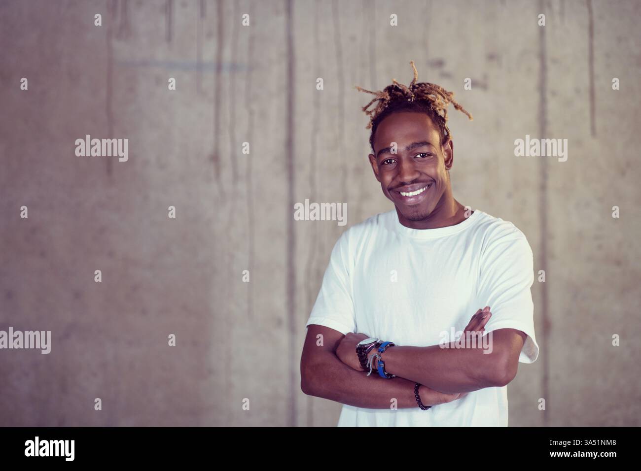 Ritratto di un giovane uomo nero americano sorridente in un abbigliamento casual, in piedi di fronte a un muro di cemento in un ufficio startup. L'atmosfera allegra e lo sfondo moderno trasmettono imprenditorialità e creatività. Ideale per affari, startup e stili di vita professionali. Foto Stock