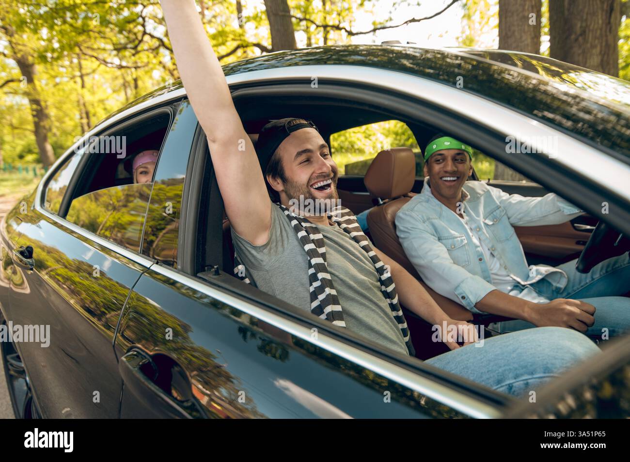 Diversi gruppi di amici sorridono e chiacchierano mentre guidano attraverso una strada nella foresta durante un viaggio su strada. Questa vivace scena su strada si adatta a viaggi, avventure e campagne di lifestyle di gruppo. Foto Stock