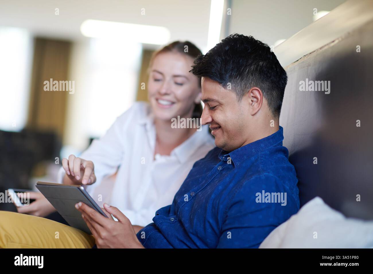 Uomo indiano che collabora con una collega donna su un tablet in una moderna area relax dell'ufficio startup. Questo ambiente diversificato e professionale si adatta al lavoro di squadra, all'innovazione e alle campagne aziendali. Foto Stock