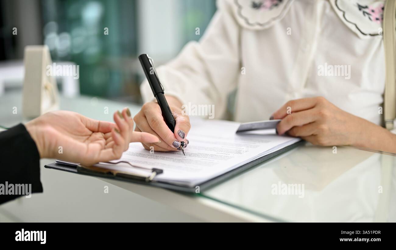 Primo piano di un ospite che compila un modulo e firma un documento alla reception dell'hotel. Ottimo per il branding del settore alberghiero, il check-in alla reception e la grafica dei servizi per gli ospiti. Foto Stock