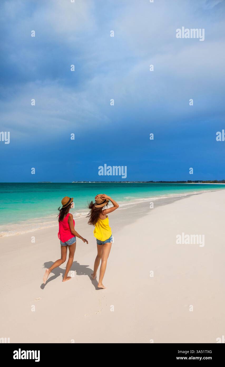 Idilliaca scena tropicale dell'isola con diversi amici che indossano cappelli Panama che camminano lungo l'oceano alle Bahamas. Questo luminoso ambiente di vacanza è ideale per viaggi, vacanze e campagne di lifestyle in spiaggia. Perfetto per destinazioni, residence e promozioni di viaggi di gruppo. Foto Stock
