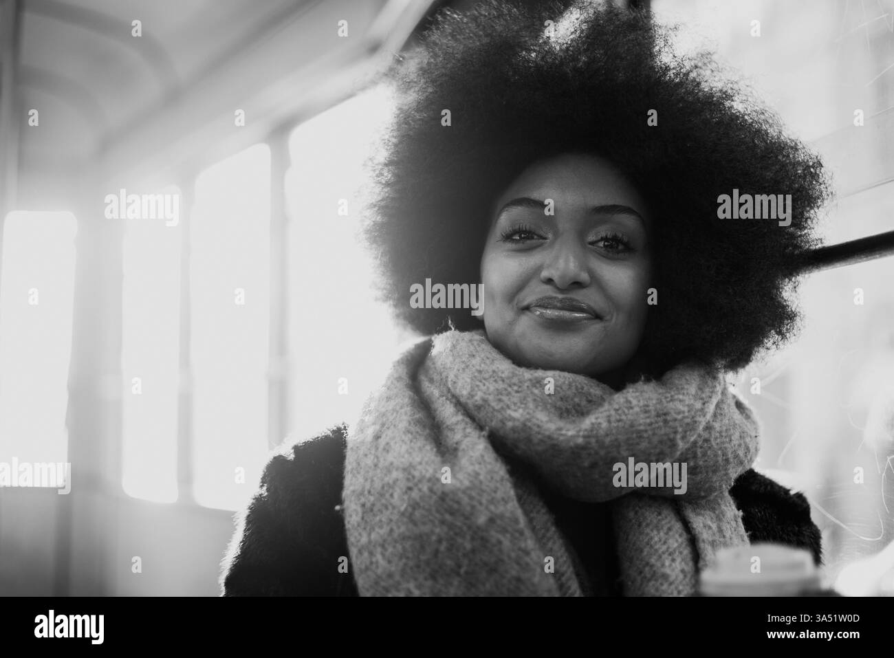 Bella donna con ritratti afro tagliati di capelli nei trasporti pubblici, che trasmette un sincero momento urbano su un autobus o un tram. Trasuda stile e fiducia nei viaggi in città e nella vita di tutti i giorni. Foto Stock