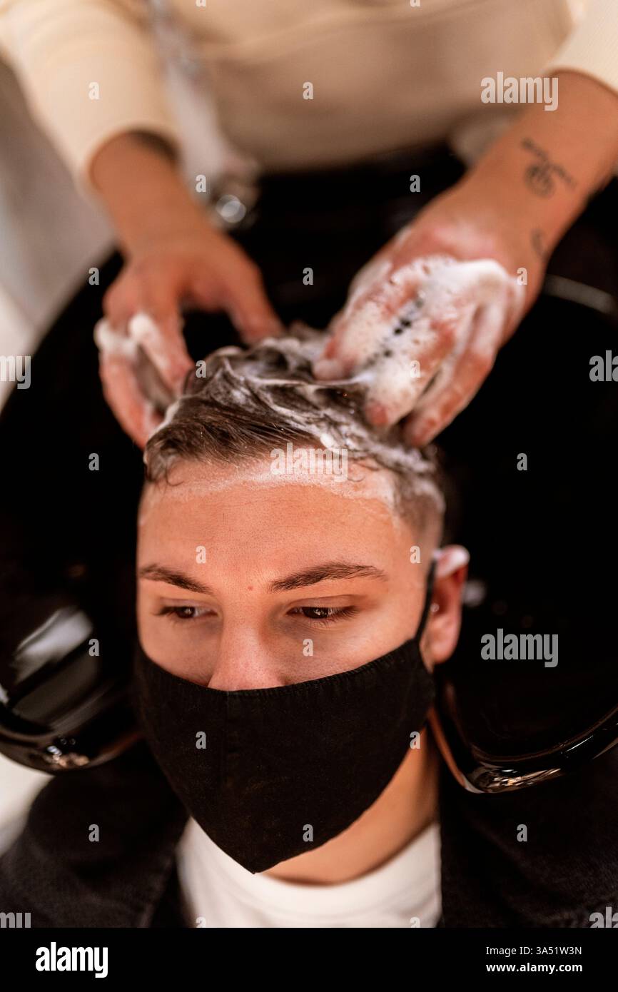 Parrucchiere ispanico che lava i capelli di un cliente maschio in un barbiere. Salone interno adatto a servizi di parrucchiere, igiene e campagne di bellezza professionali. Foto Stock
