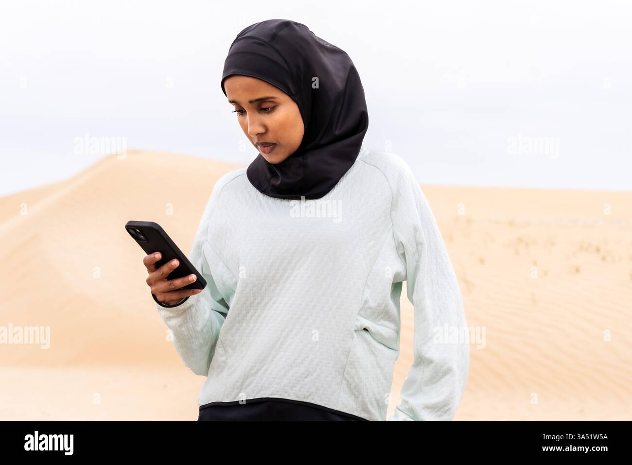 Una donna araba atletica che indossa un hijab si allena all'aperto in un ambiente desertico. Immagini sportive e fitness con abbigliamento sportivo e burkini modesti. Ideale per campagne di benessere e grafica per lo stile di vita in Medio Oriente. Foto Stock