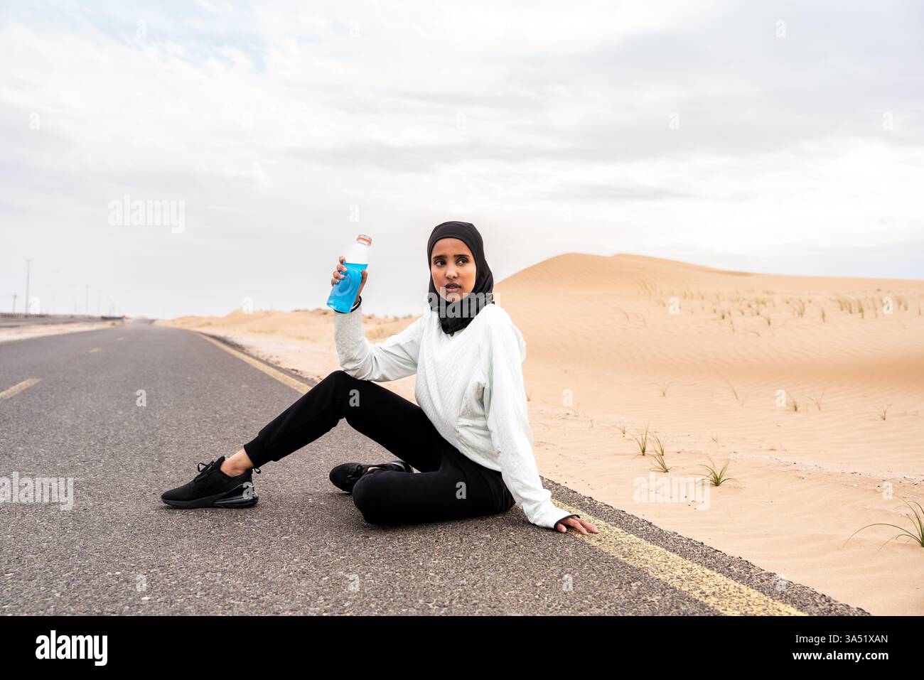 Donna araba del Medio Oriente sportiva in hijab che si allena all'aperto in un ambiente desertico, indossando abbigliamento sportivo burkini. Questa immagine di benessere atletico si adatta alle campagne di fitness, alle attività all'aperto e alle promozioni sull'abbigliamento sportivo. Foto Stock