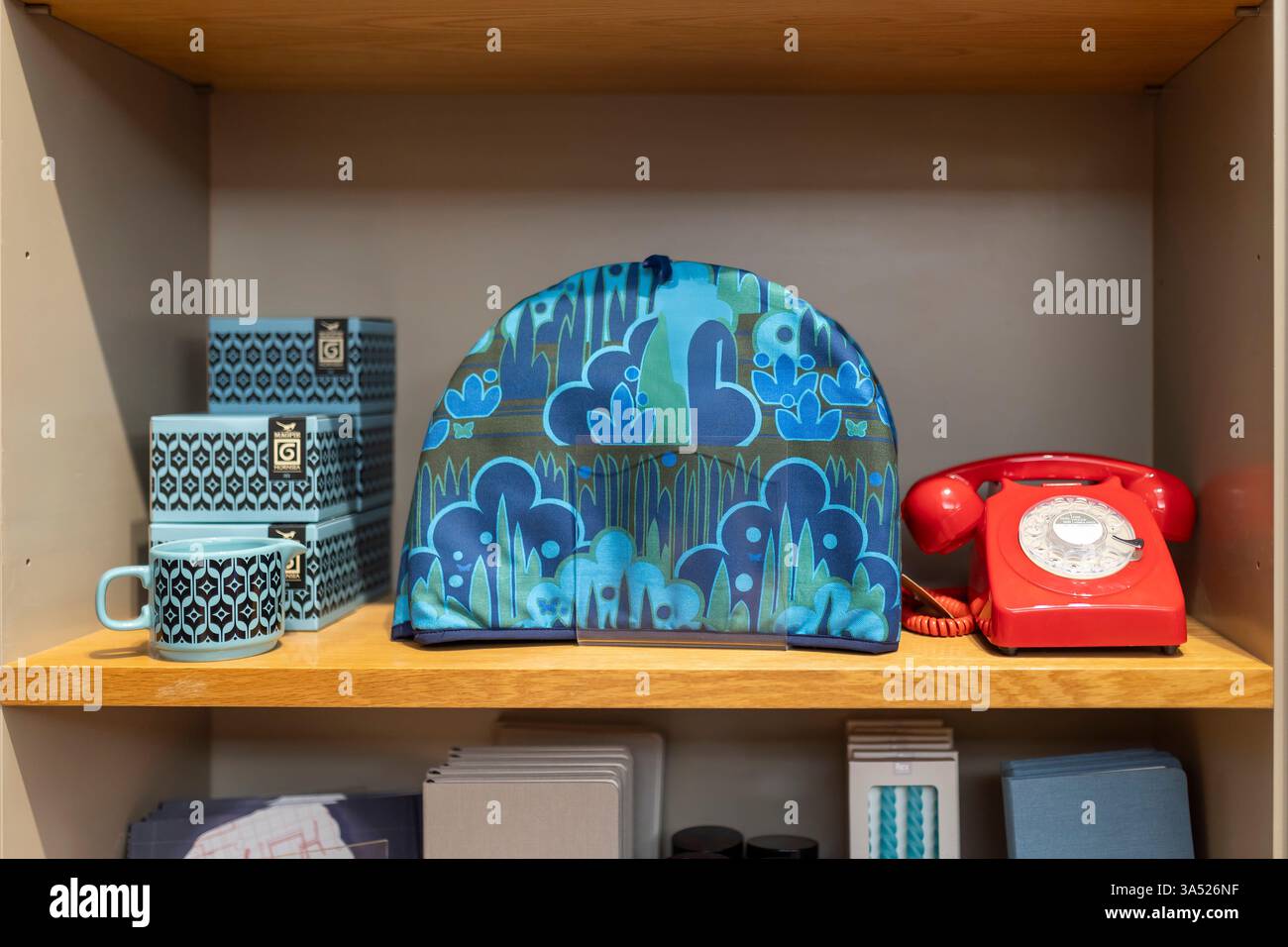Londra, Regno Unito - 1 dicembre 2024: Un vecchio telefono rotativo rosso con un cavo, una borsa con un design a marchio e tazze nel Museum of the Home. Foto Stock
