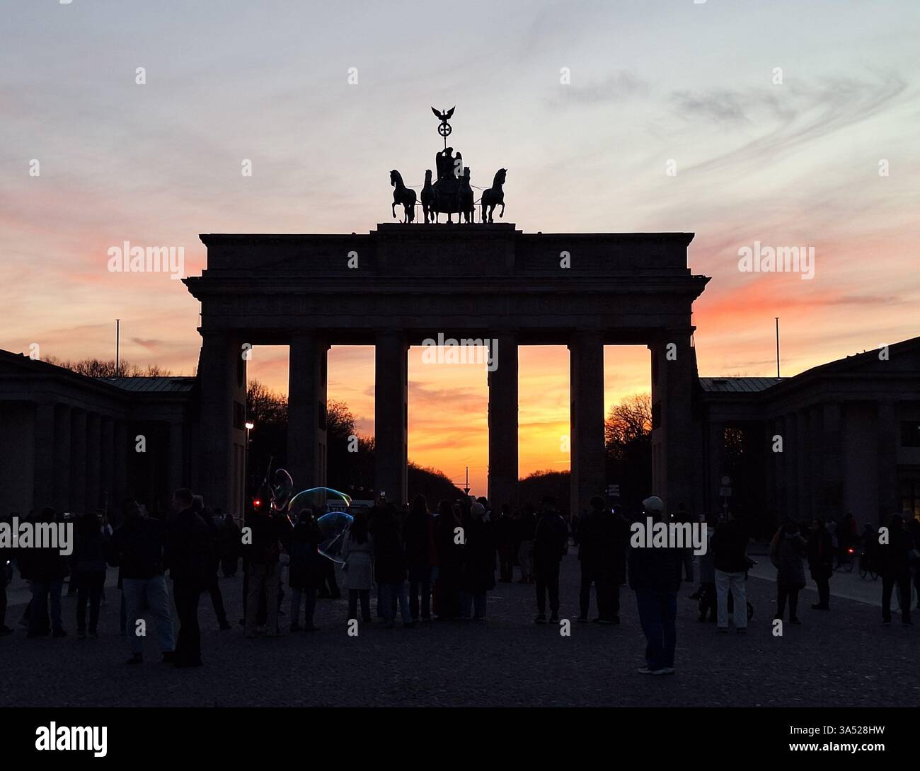 I turisti si allineano di fronte al simbolo Brandenburger Tor (porta di Brandeburgo) per guardare il colorato tramonto sul parco Tiergarten, Berlino, Germania Foto Stock