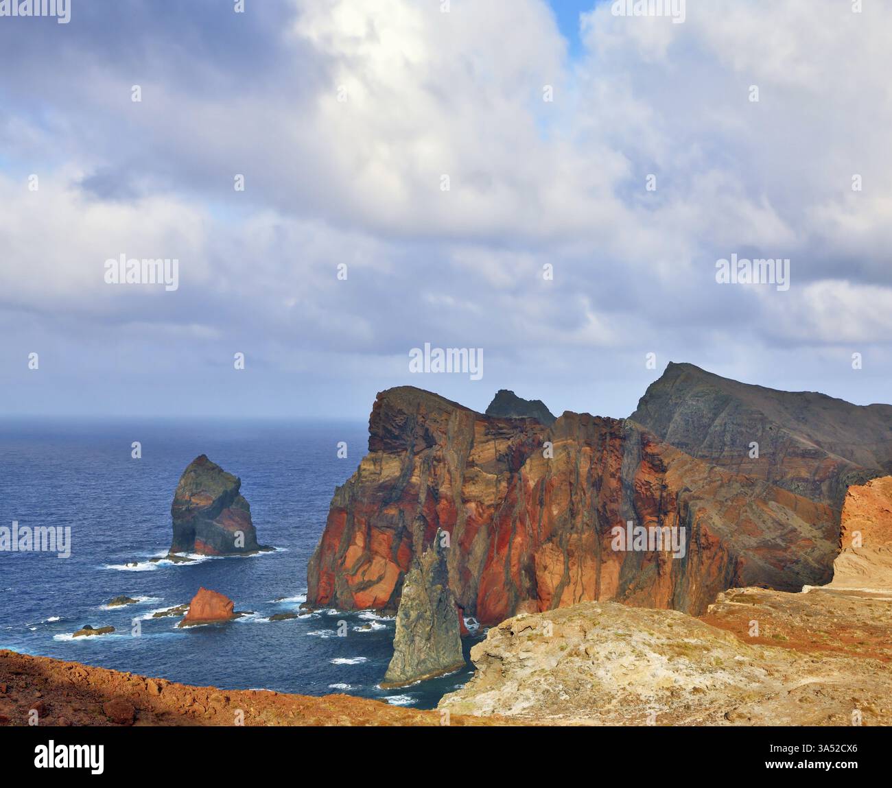 Le rocce rosse e arancioni crescono freddamente dalle onde schiumose dell'Oceano Atlantico. Punta più orientale dell'isola di Madeira Foto Stock