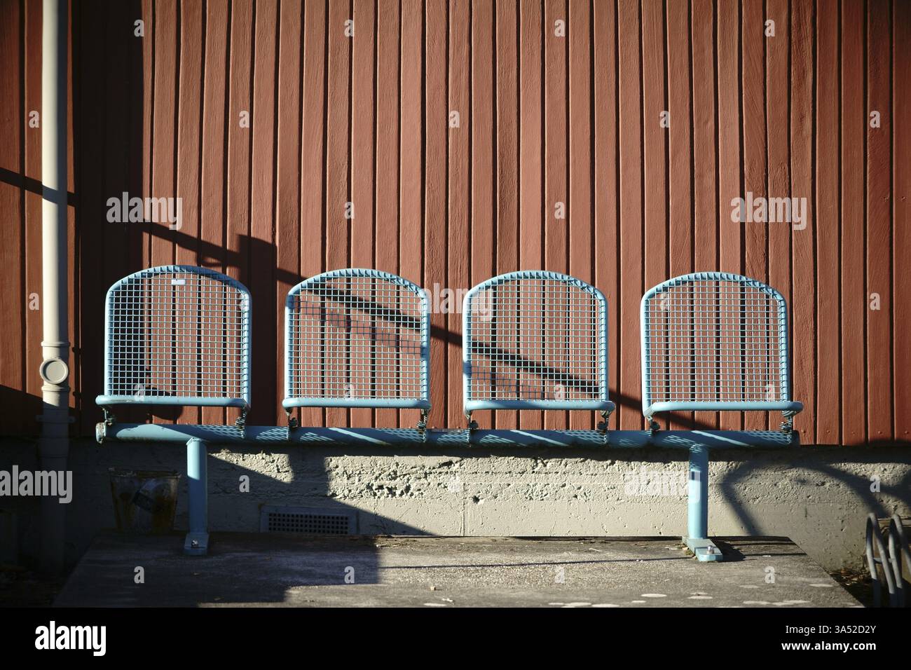 Posti a sedere allineati uno accanto all'altro di fronte ad una facciata in legno alla luce del sole Foto Stock