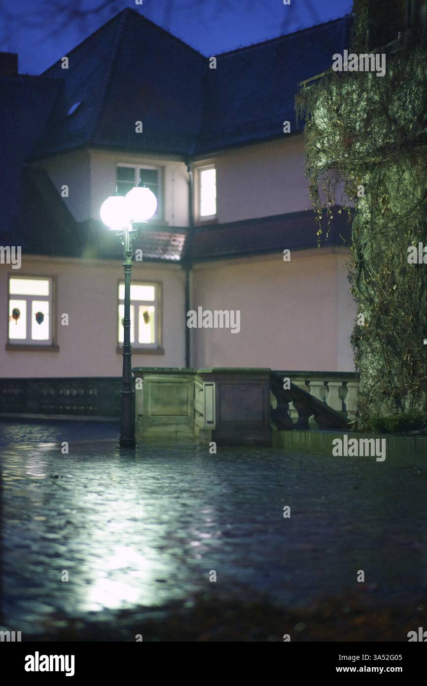 Le luci delle Lanterne illuminano una stretta piazza piovosa di fronte a un edificio residenziale Foto Stock