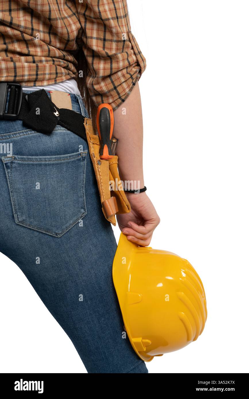 Una vista ravvicinata della vita di un operaio edile, che mostra una cintura portautensili con vari utensili e un elmetto giallo tenuto in una mano, a simboleggiare la sicurezza e la sicurezza Foto Stock