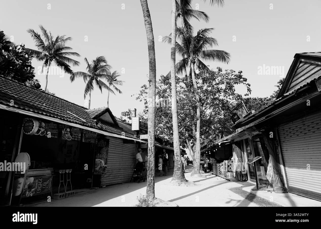 Il sole sorge su una strada tropicale con alcuni negozi che aprono presto e torreggianti palme Foto Stock