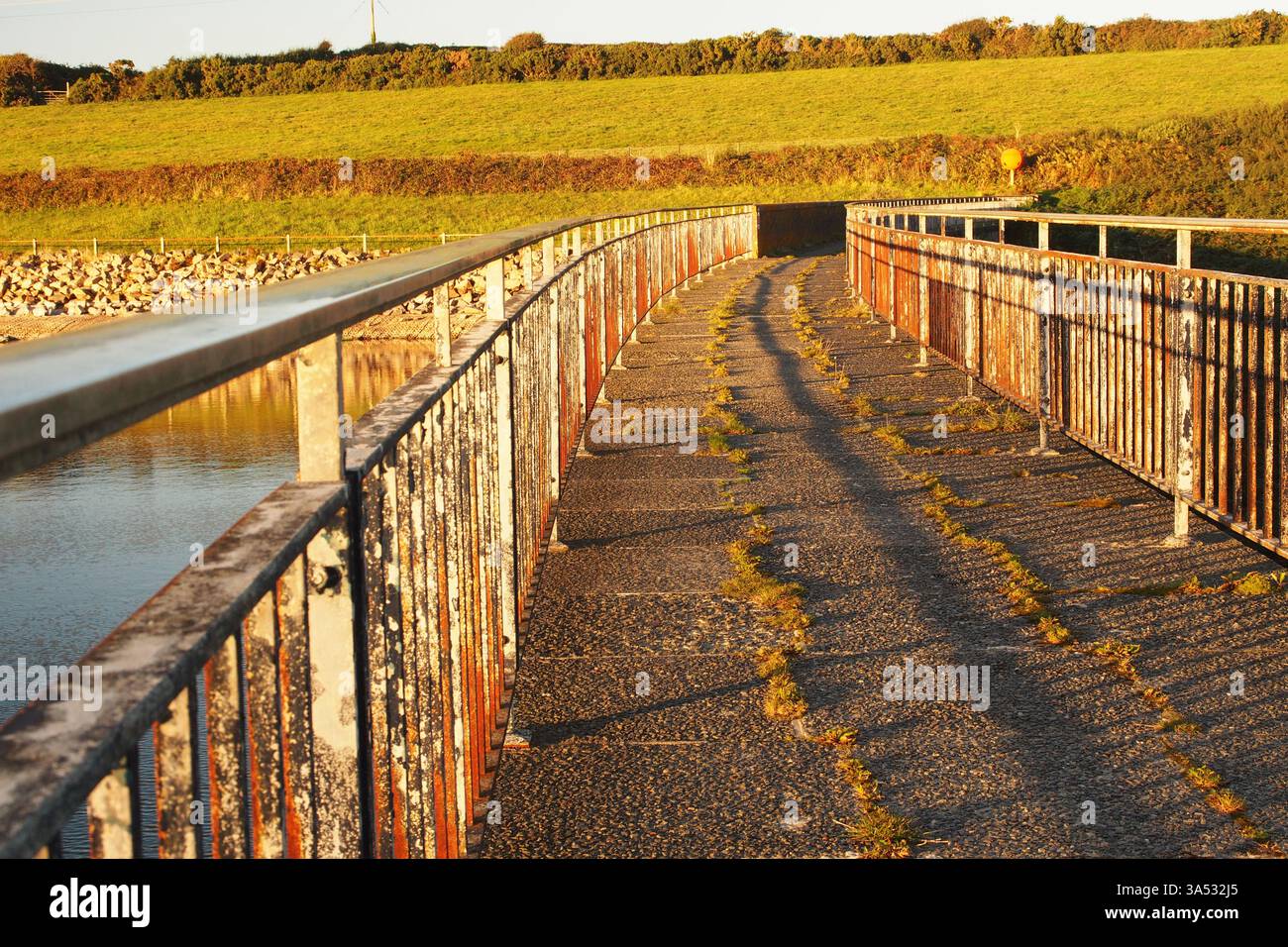 Passerella pedonale della diga del serbatoio, con ringhiere in ferro, ombre serali e sole a Drift, Cornovaglia, Inghilterra Regno Unito Foto Stock