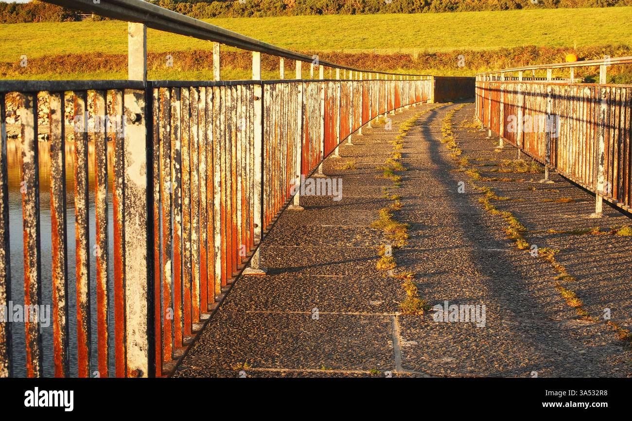 Passerella pedonale della diga del serbatoio, con ringhiere in ferro, ombre serali e sole a Drift, Cornovaglia, Inghilterra Regno Unito Foto Stock