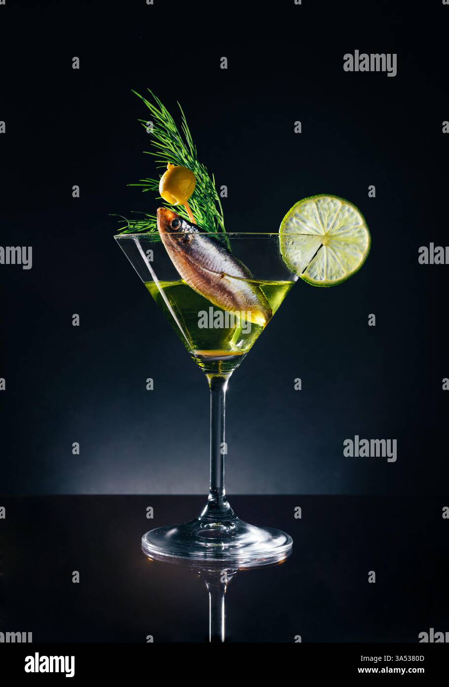 Un cocktail creativo servito in un bicchiere di martini, caratterizzato da un pesce sommerso in liquido, guarnito con lime, aneto e un'oliva. Foto Stock