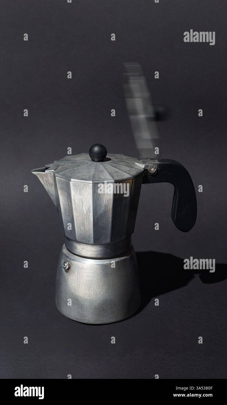 Una vecchia moka in alluminio con coperchio sfocato in movimento, catturata su uno sfondo scuro, che simboleggia l'energia e la routine del caffè mattutino. Foto Stock