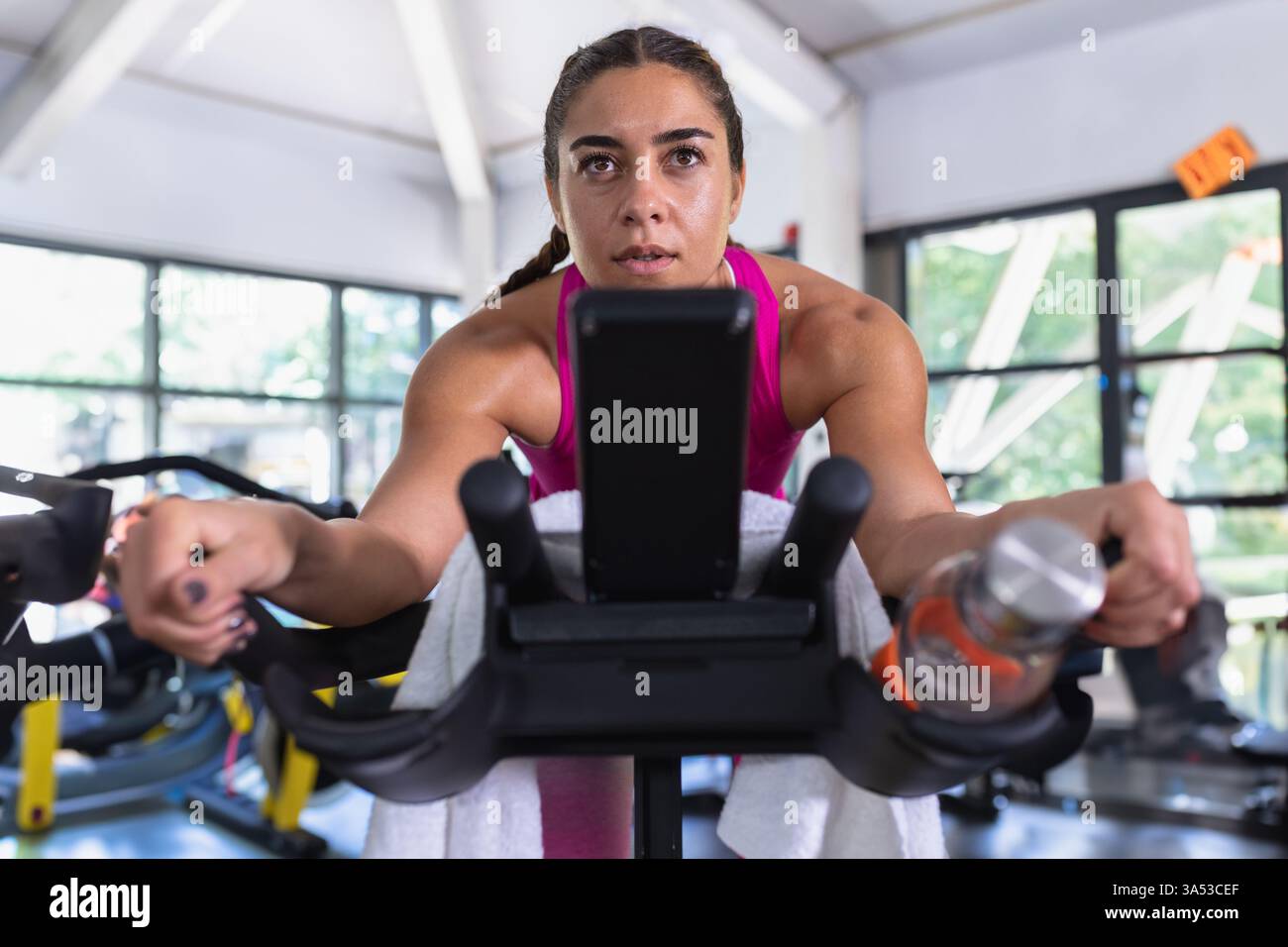 Donna concentrata che si allena con una cyclette in palestra, utilizzando lo smartphone per motivare Foto Stock