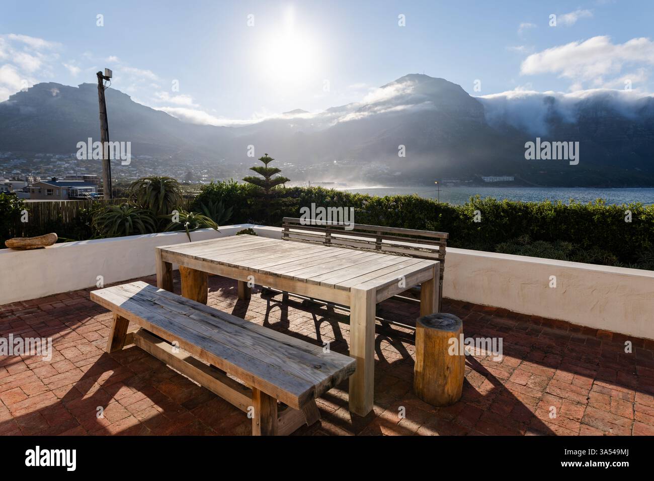 Tavolo in legno sul patio illuminato dal sole con vista sulle montagne e sull'oceano, ideale per rilassarsi, spazio fotocopie Foto Stock