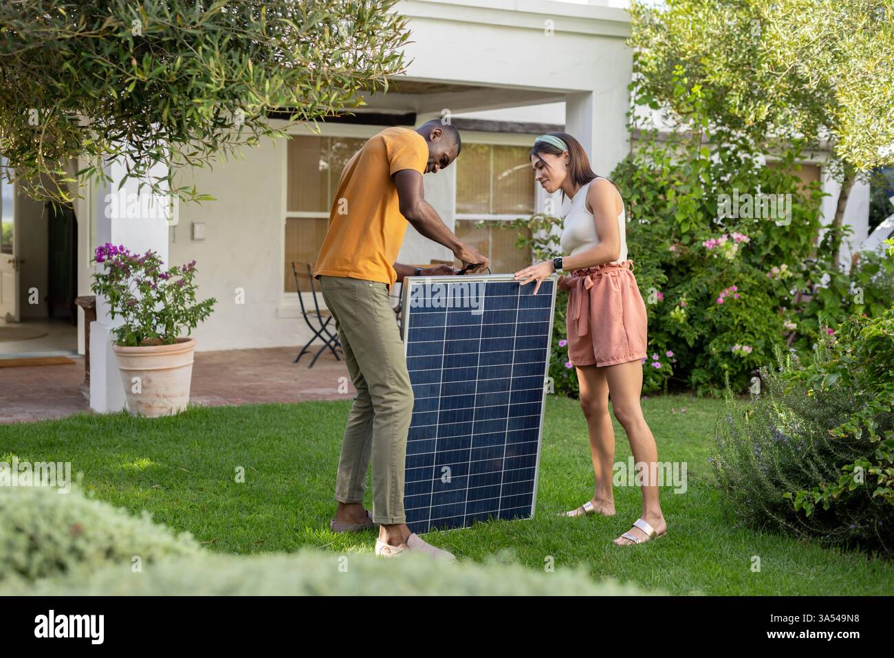 Diverse coppie installano pannelli solari in giardino, godendo di una vita sostenibile in vacanza Foto Stock