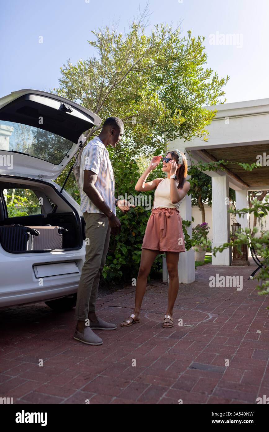 Coppia eterogenea che si diverte in vacanza, donna che scatta foto con lo smartphone vicino all'auto all'aperto Foto Stock