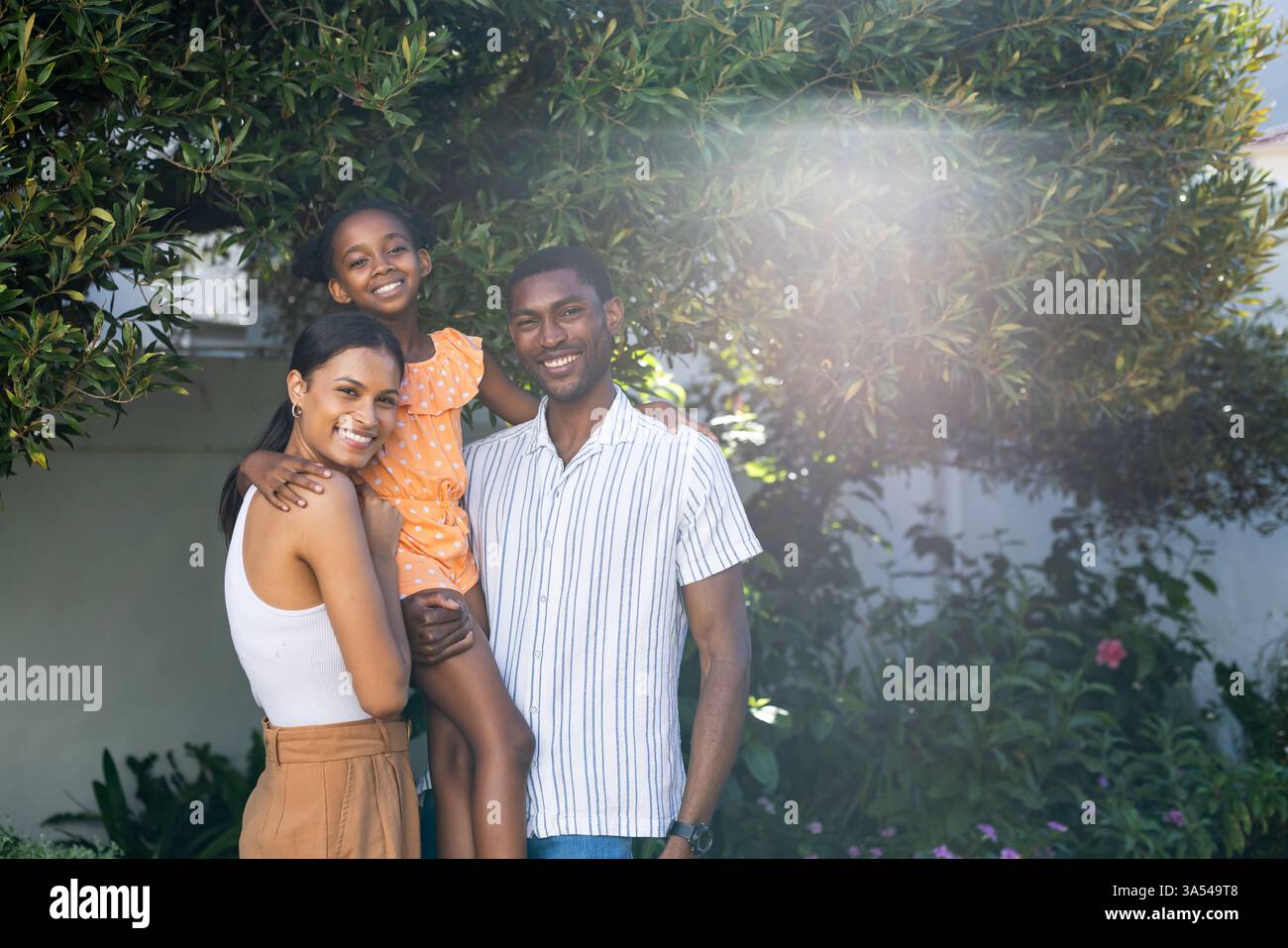 Famiglia sorridente che si gode una vacanza all'aperto, figlia in abito arancione tenuta Foto Stock