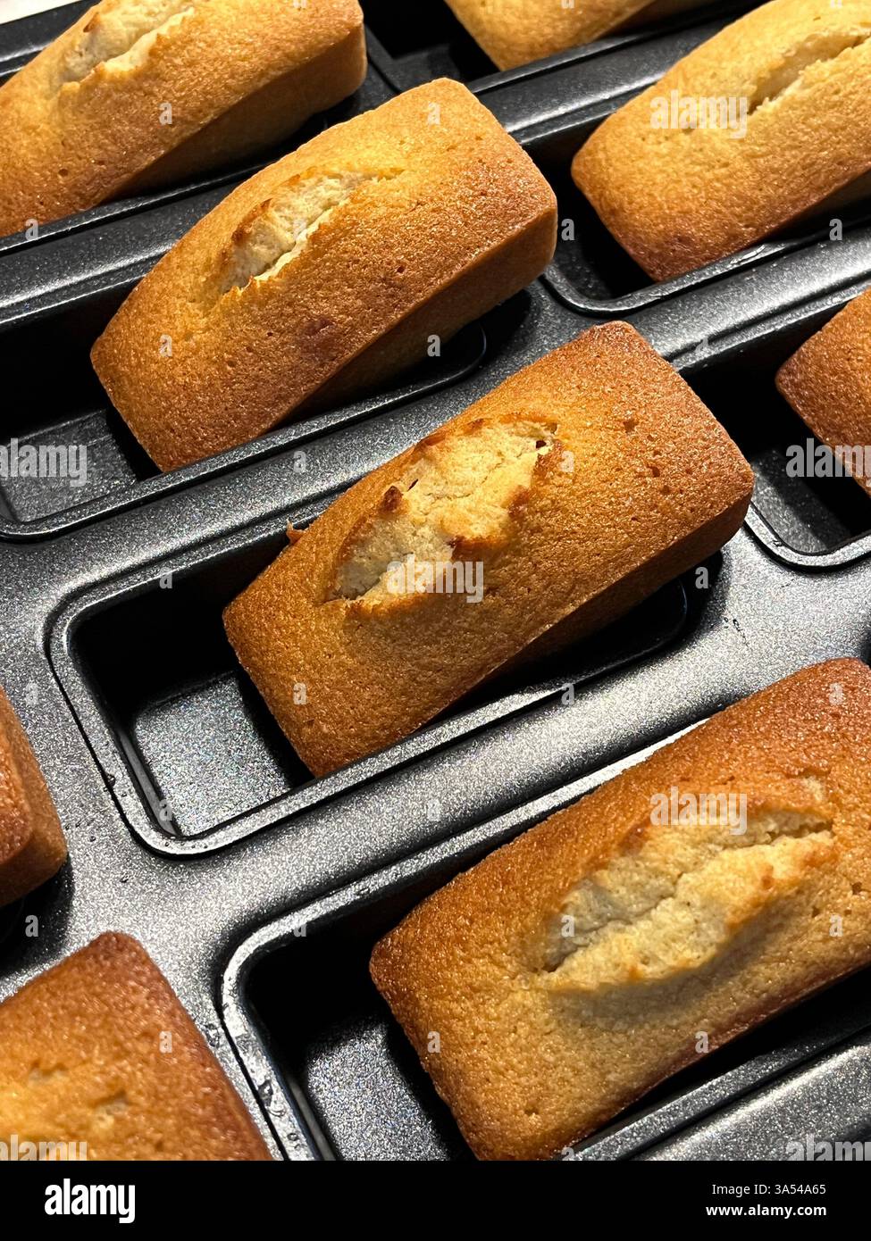 Primo piano di finanzieri dorati appena sfornati in un vassoio da forno, tradizionali torte di mandorle francesi con un bordo croccante e un centro umido. Foto Stock