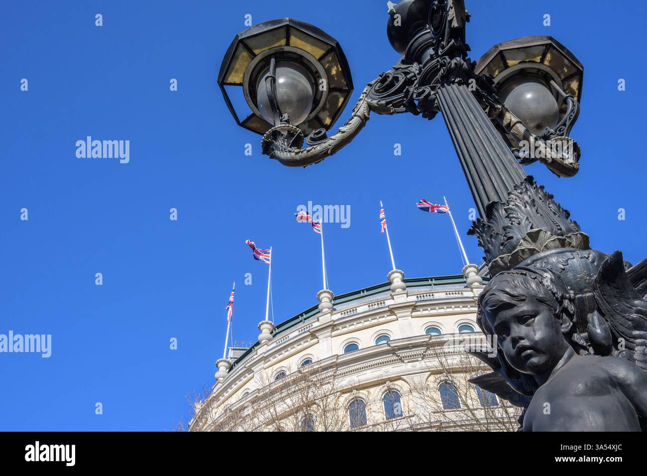 Londra, Regno Unito. Palo della lampada in Trafalgar Square (con un "cherubino piangente") e bandiere dell'Unione che sventolano dal tetto del "Grand Building" all'angolo con Foto Stock