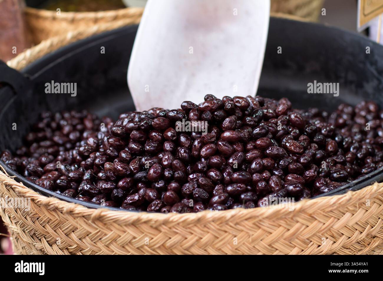 Primo piano di un cesto di vimini pieno di olive nere in un mercato all'aperto. Un prodotto di esportazione spagnolo, apprezzato in gastronomia e salute. Commercio globale e. Foto Stock