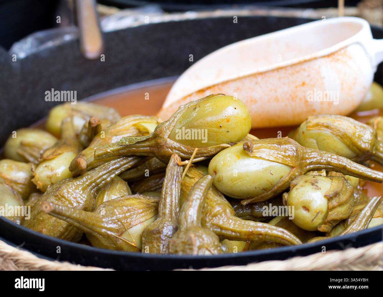 Primo piano di melanzane sottaceto in una padella con liquido marinato e un cucchiaio bianco da portata. Cibo tradizionale conservato con spezie. Foto Stock