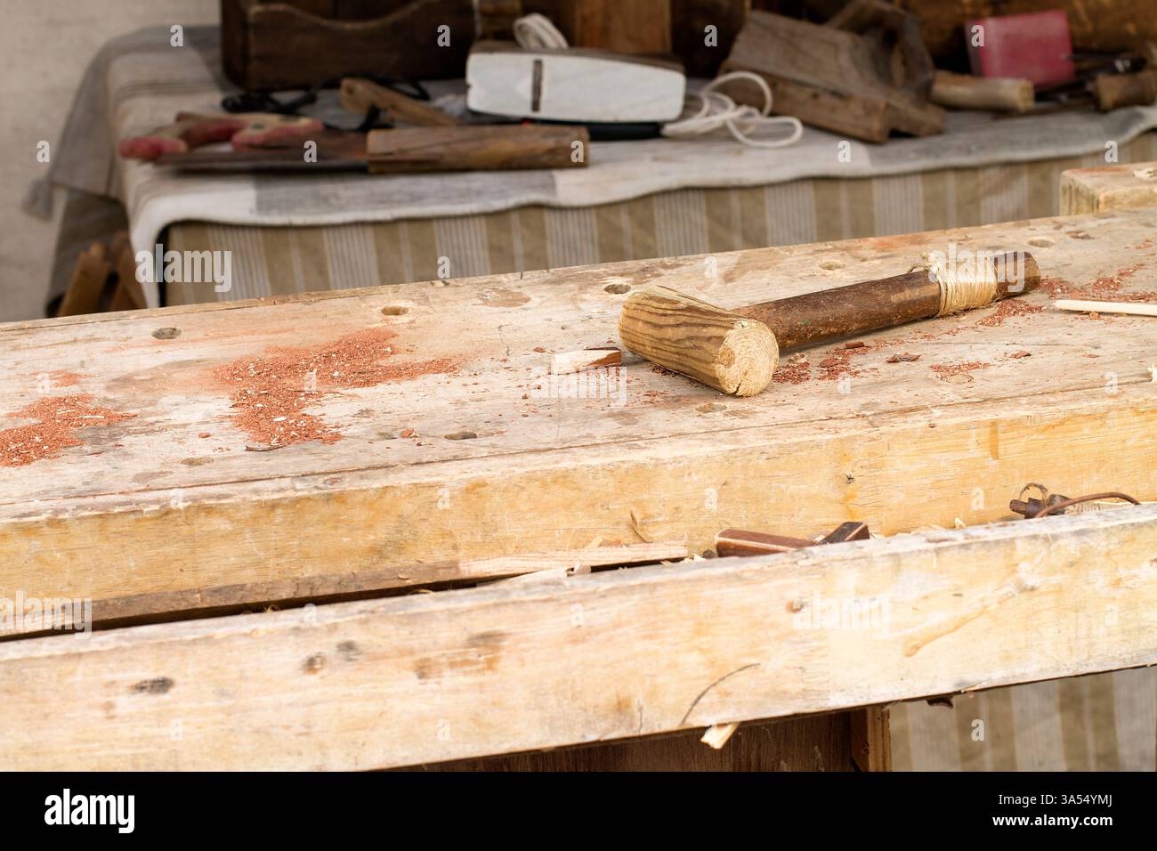 Banco da lavoro per falegname con utensili per la lavorazione del legno, tra cui un mazzuolo in legno realizzato a mano, ricoperto di segatura e trucioli di legno. Sullo sfondo, più trad Foto Stock