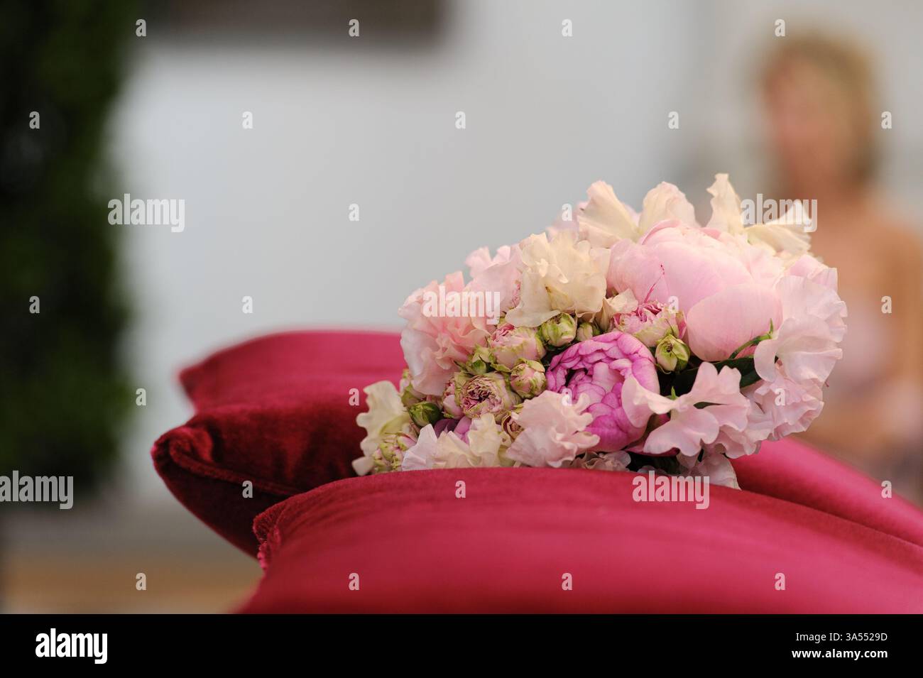 Elegante bouquet di fiori rosa posto sopra lussuosi cuscini in velluto rosso, perfetto per matrimoni, amore o temi di arredamento. Foto Stock