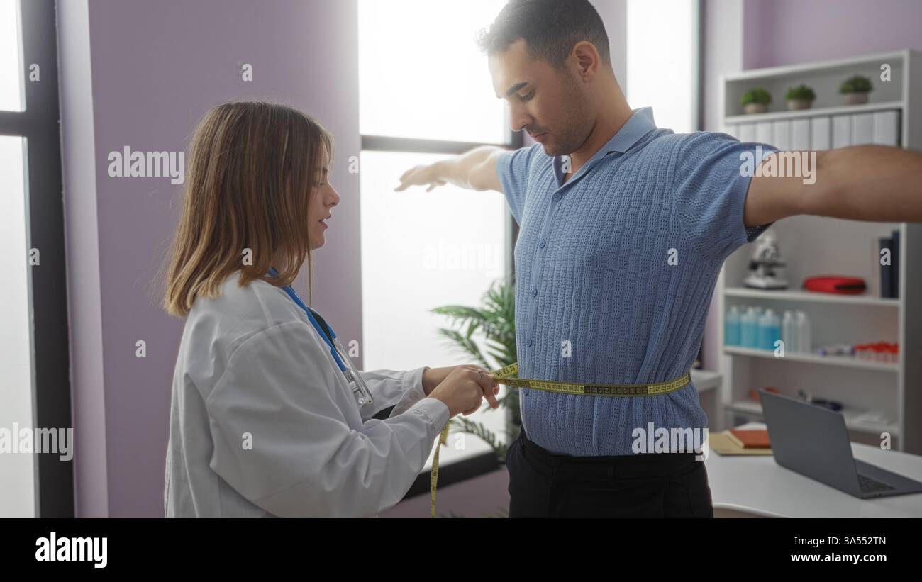 Donna uomo di misurazione con nastro in clinica che indossa stetoscopio in sala esame medica concentrandosi su controllo sanitario in interni. Foto Stock