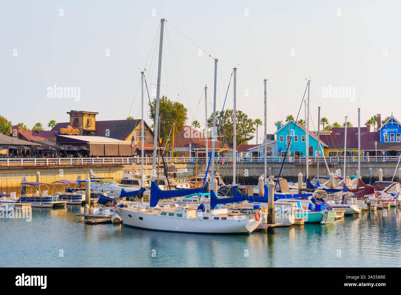 Long Beach, California - 11 gennaio 2025: Barche a vela colorate sono ormeggiate nel Rainbow Harbor, circondato da ristoranti e negozi sul lungomare di The Shor Foto Stock