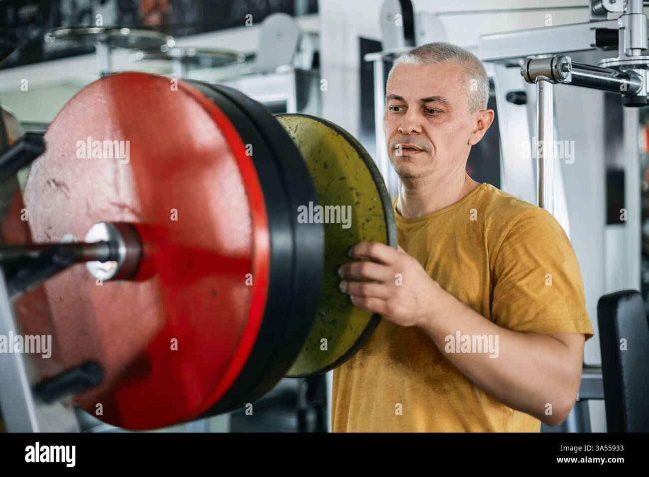 Uomo muscoloso calvo che carica le piastre di peso su un barbell in palestra Foto Stock
