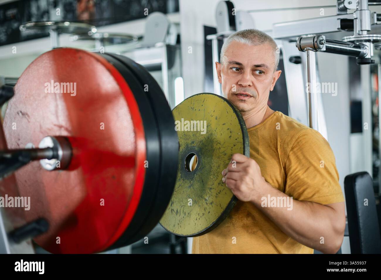 Uomo muscoloso calvo che prepara i pesi per un barbell in palestra Foto Stock
