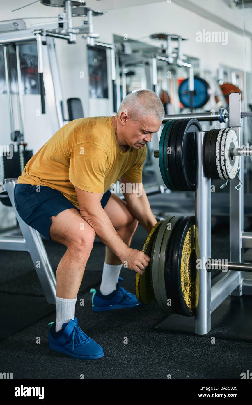 Uomo muscoloso calvo che organizza i pesi in palestra Foto Stock
