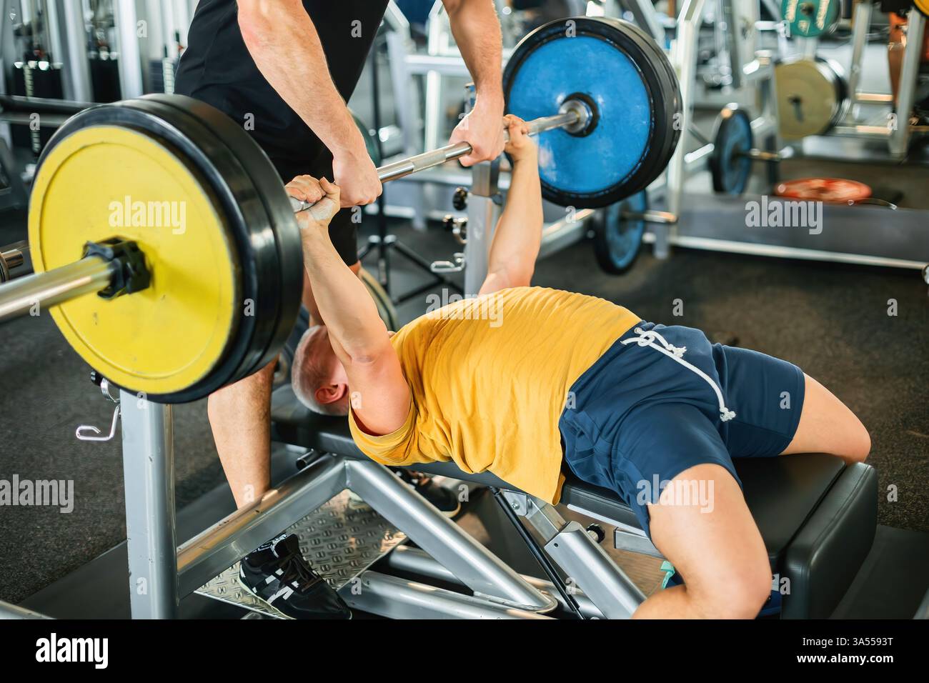 L'atleta esegue con sicurezza la pressa da banco con il supporto dell'allenatore Foto Stock
